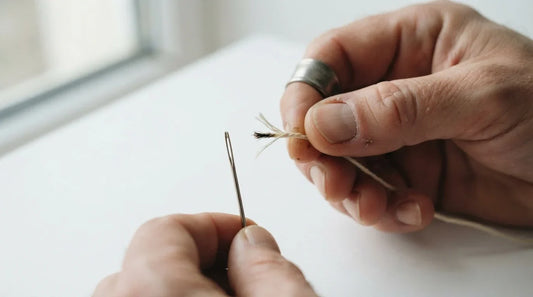 Hands wet-twisting thread tip to thread a sewing needle.